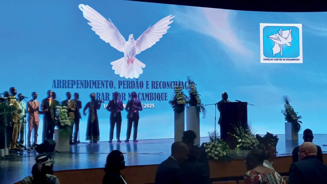 A line of people stand on a stage with a large screen behind then projecting a dove.