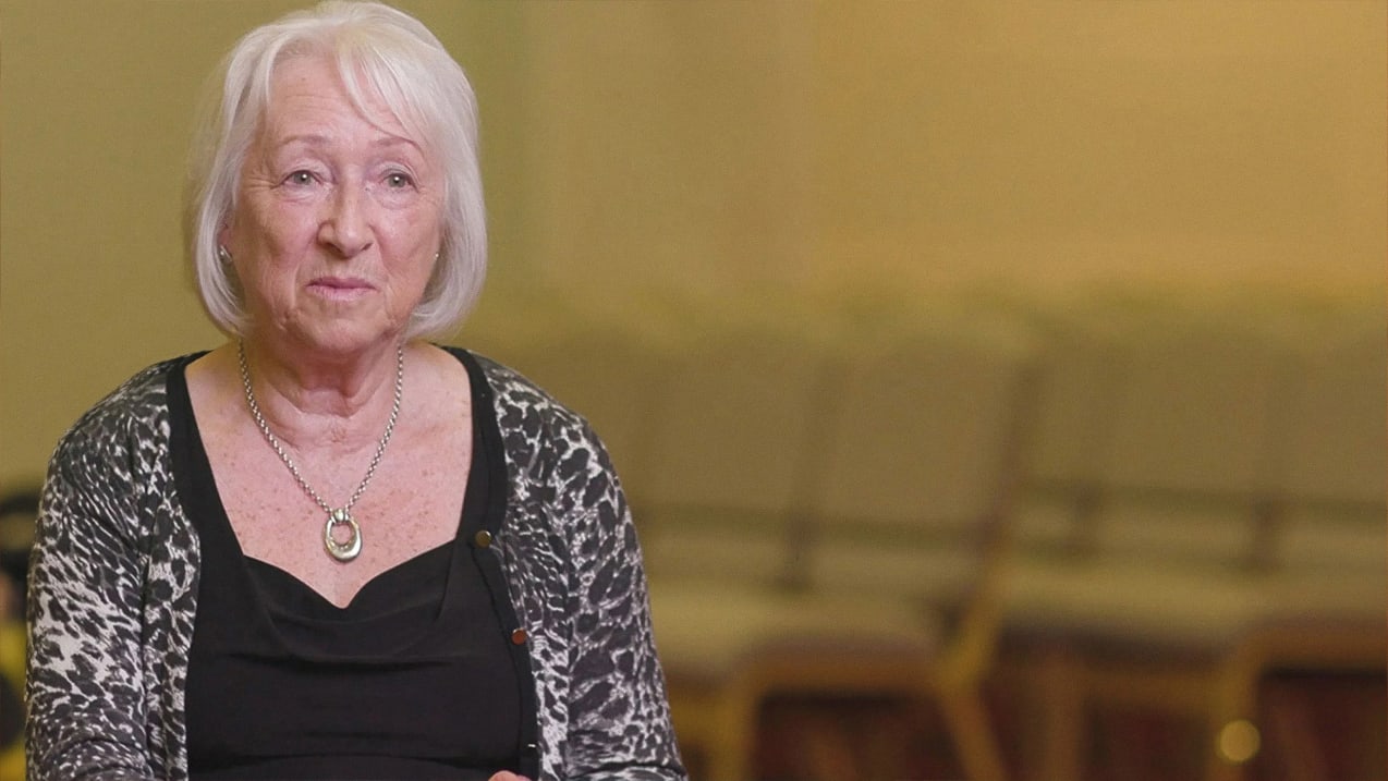 Portrait of older white-haired woman with necklace wearing a black top and animal print sweater.