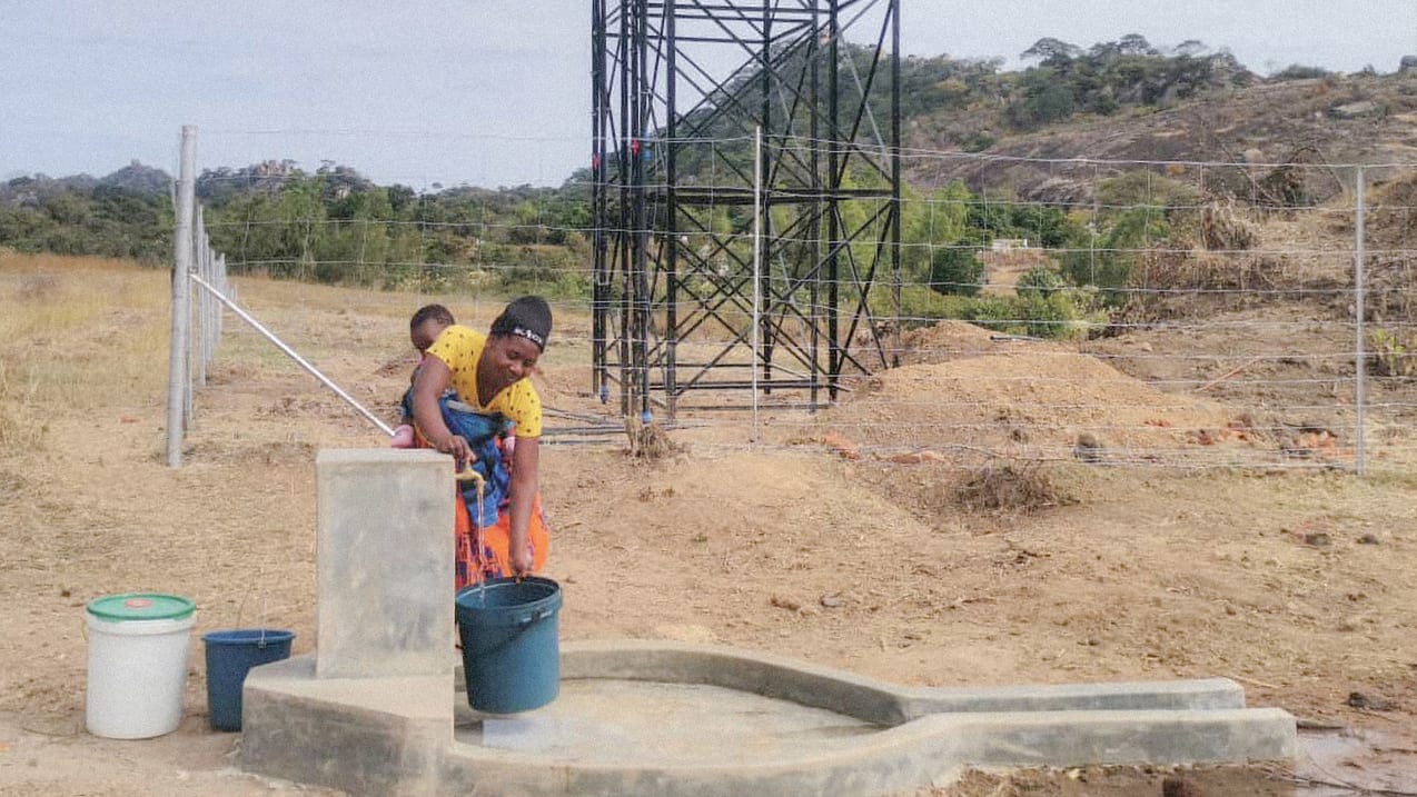 Woman and child drawing water from well near a cell tower in a rural environment.