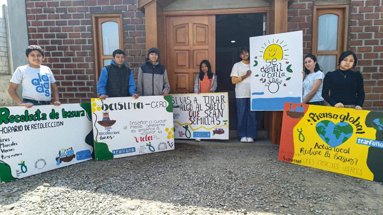 A group of children hold up hand painted signs in front of a brick building.