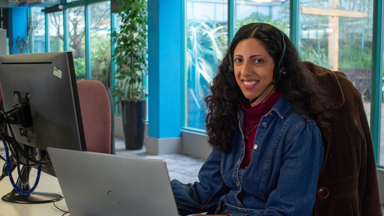 A smiling woman sitting at a desk in an office wearing a headset