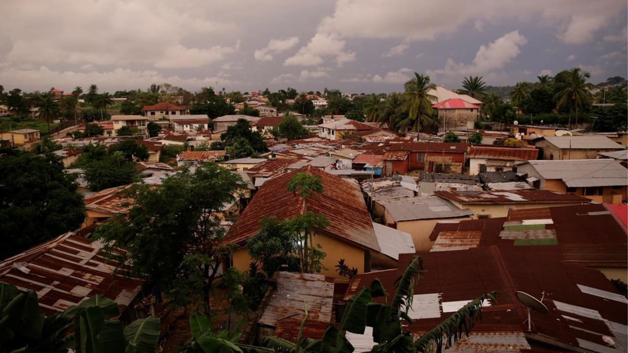 Overhead view of a dense village with rusty rooftops under a cloudy, grey sky.