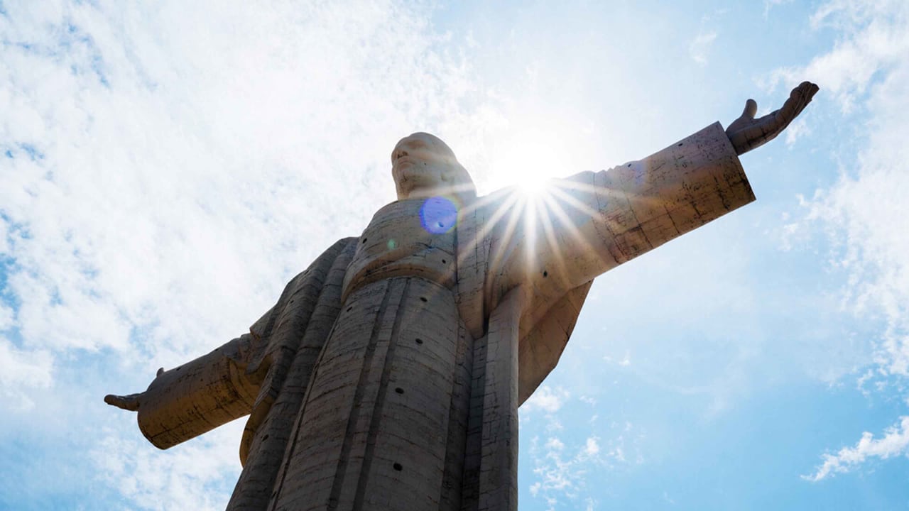 Low angle view of the Cristo de la Concordia statue with a bright sunburst behind the head.