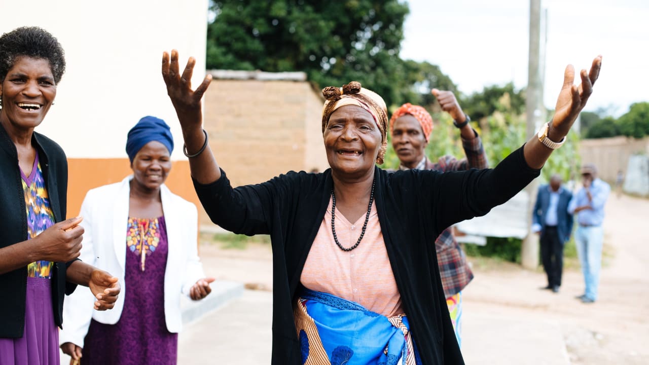 Una mujer de un grupo comunitario de mujeres en Angola sonríe elevando las manos en el aire, rodeada de otras tres mujeres