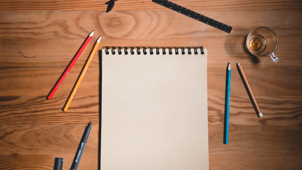 A blank sheet of paper on a desk with pens and pencils scattered around