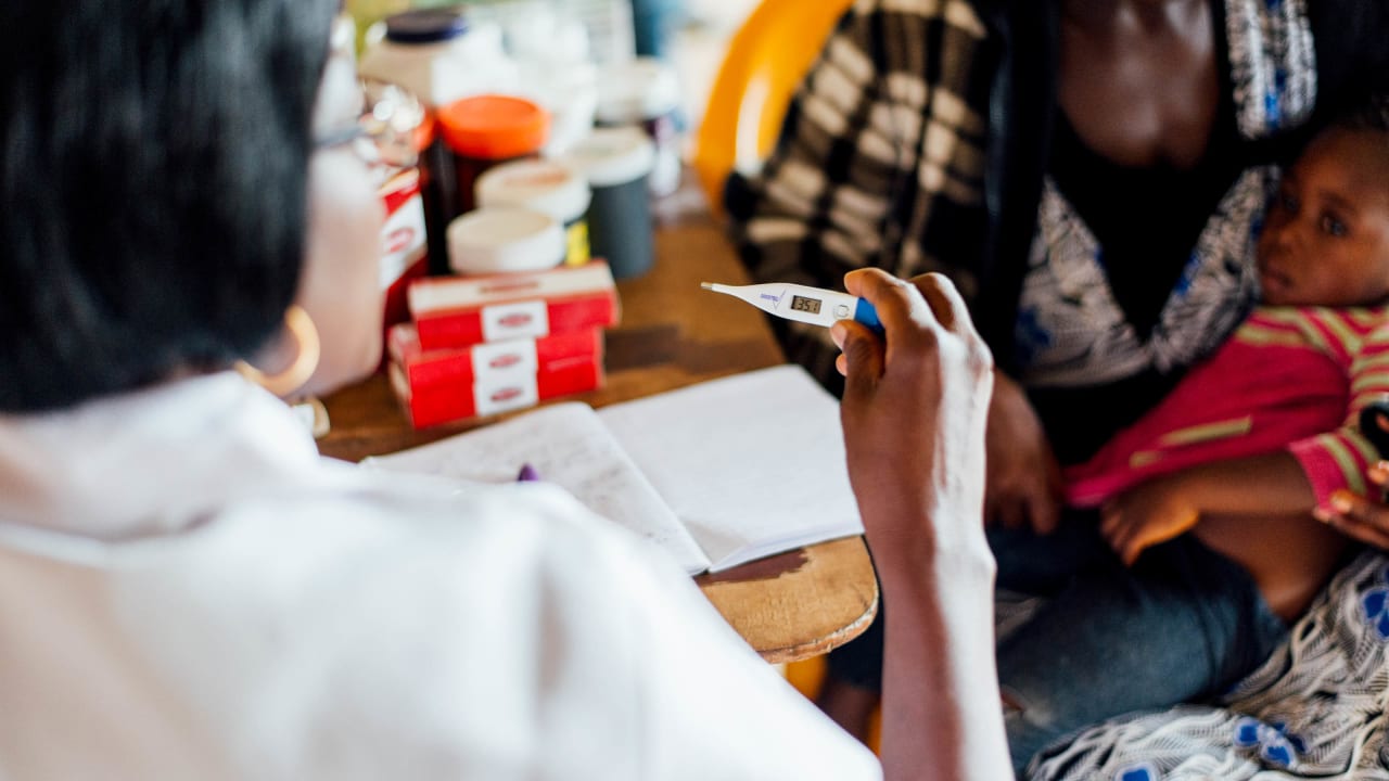 La femme en laboratoire blanche lit le thermomètre utilisé pour mesurer la température d'un enfant en détresse, qui est détenu par leur mère