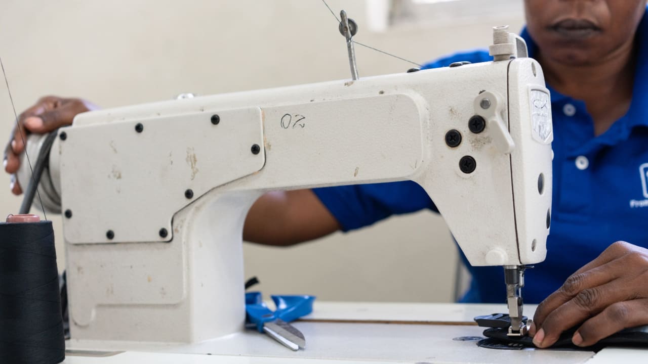Una mujer con camiseta azul cose una tela en una máquina de coser