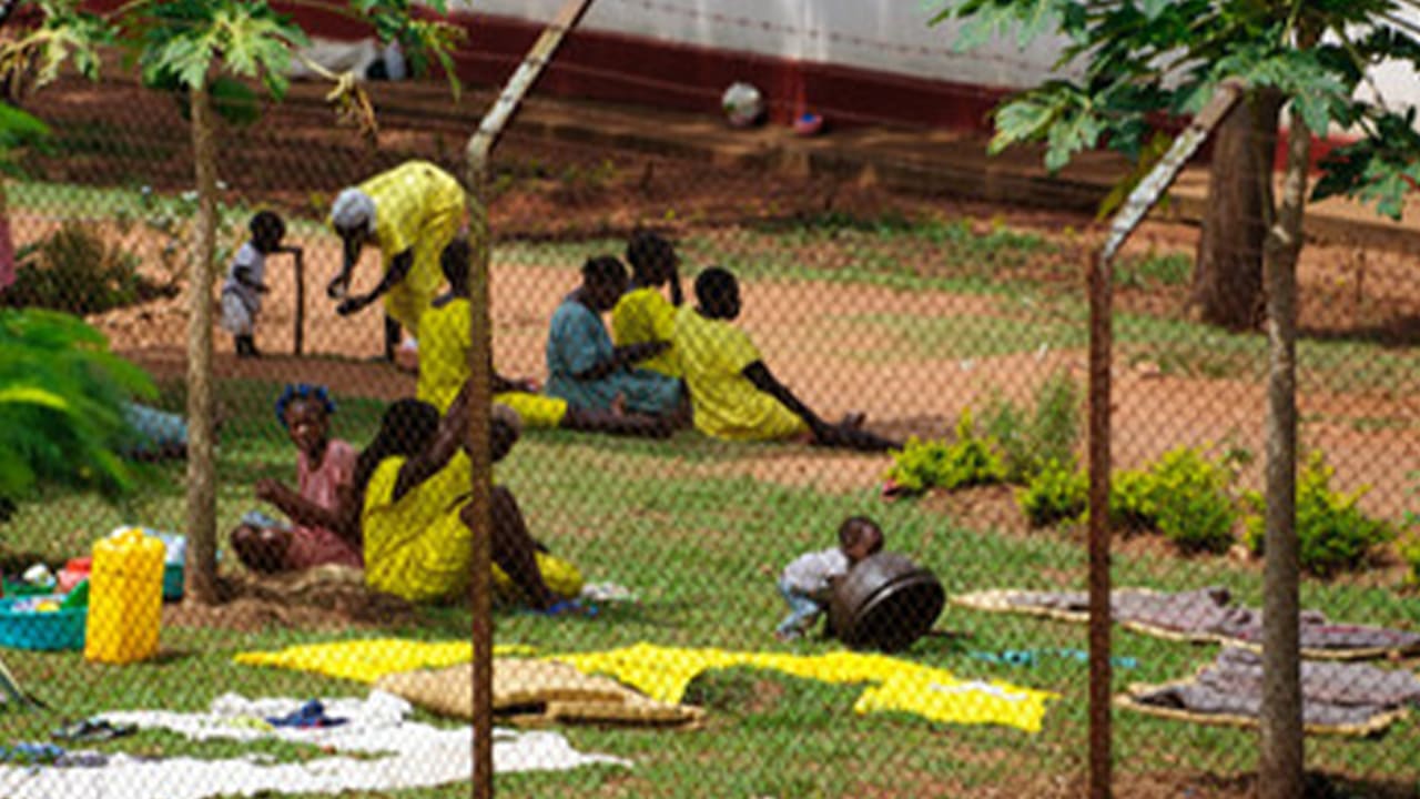 Female inmates from a prison in Uganda sit on a grassy area with a metal wire fence around it