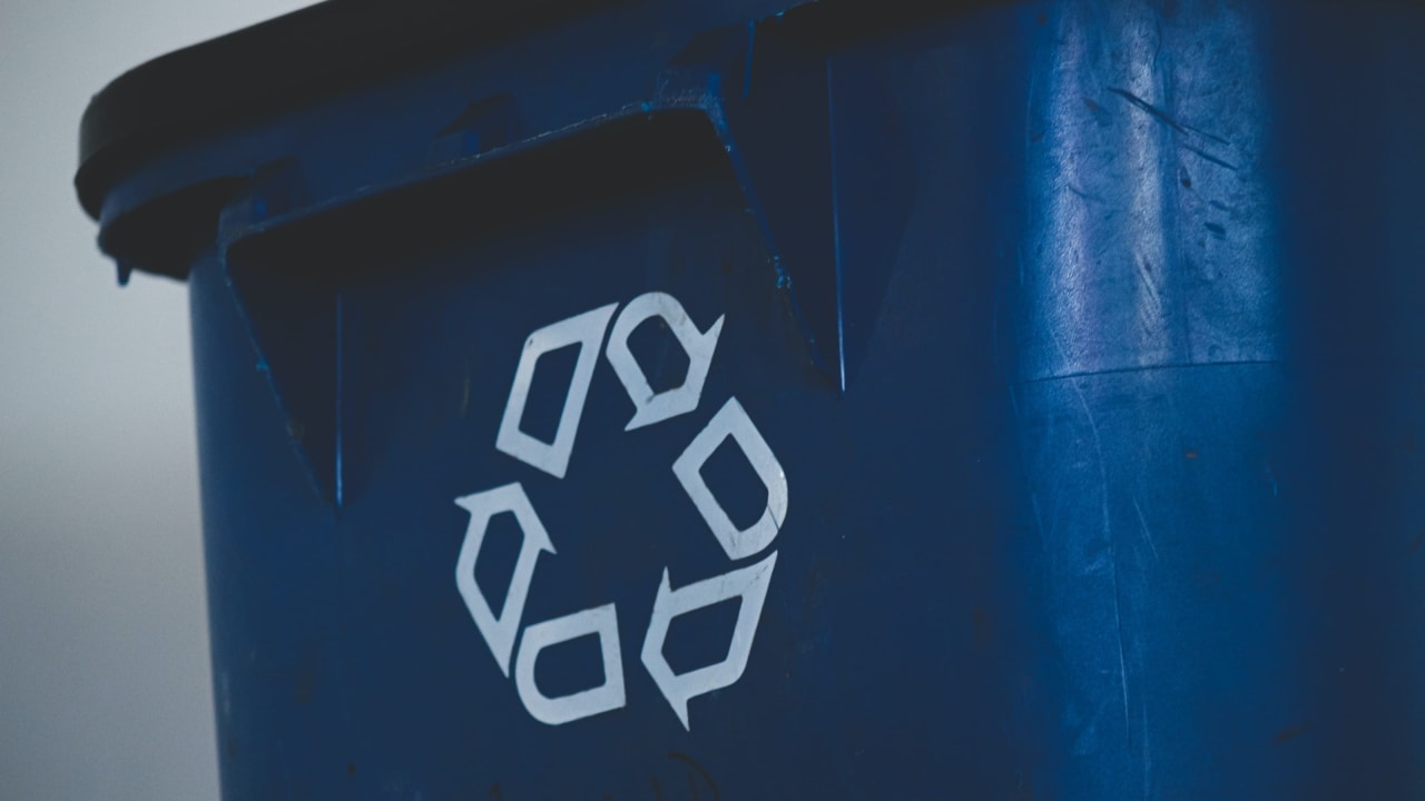 Une poubelle noire en plastique comportant le logo du recyclage au milieu.