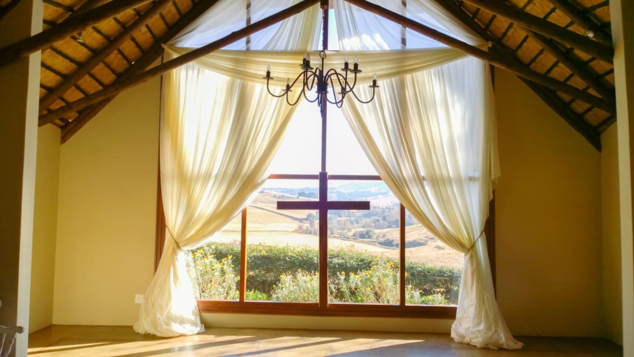 Vista de un valle en Sudáfrica a través de una ventana con un crucifijo colgando en una pequeña iglesia