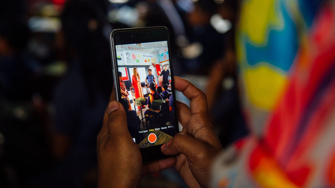 A view of a smartphone looking over the shoulder of a Bangladeshi woman