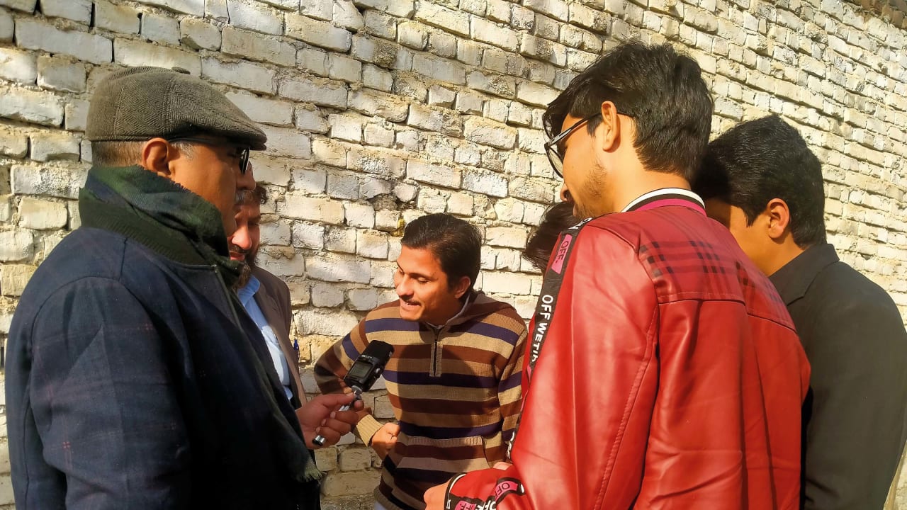 A group of men in Pakistan stand in a circle and one of them practises speaking into a microphone