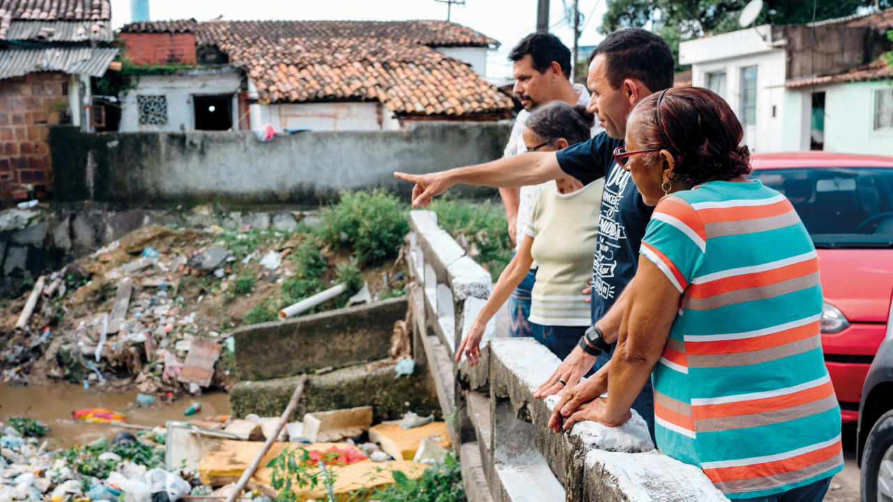 Four community members standing on a bridge looking down on the heavily polluted Tejipió River in Recife, Brazil