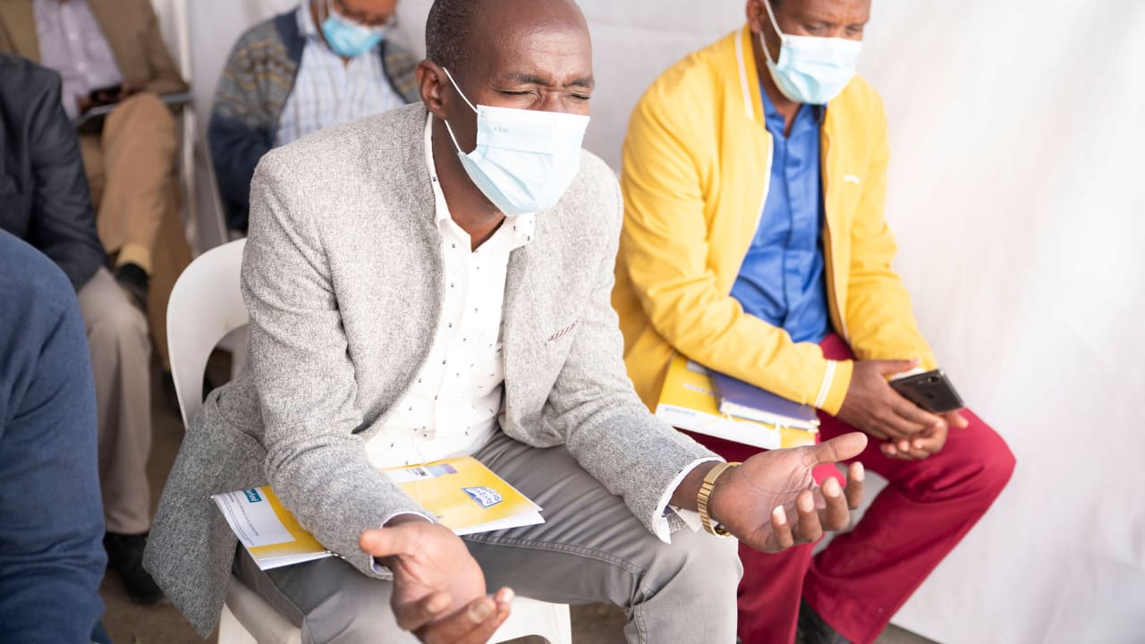 A seated man wearing a face mask praying intently in a church setting