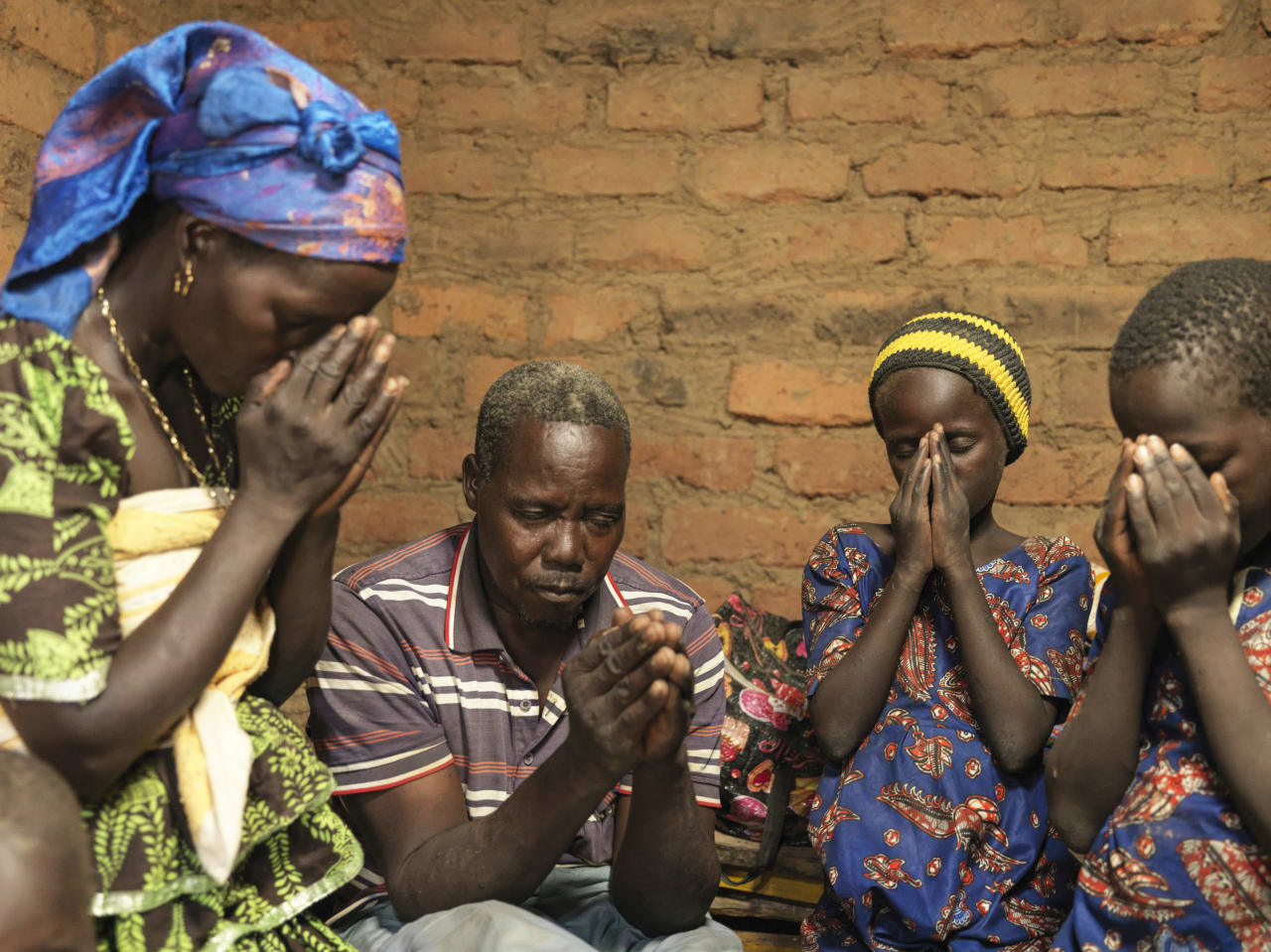 Au Tchad, une famille de quatre personnes prie les mains jointes devant leur visage, devant un mur en briques.