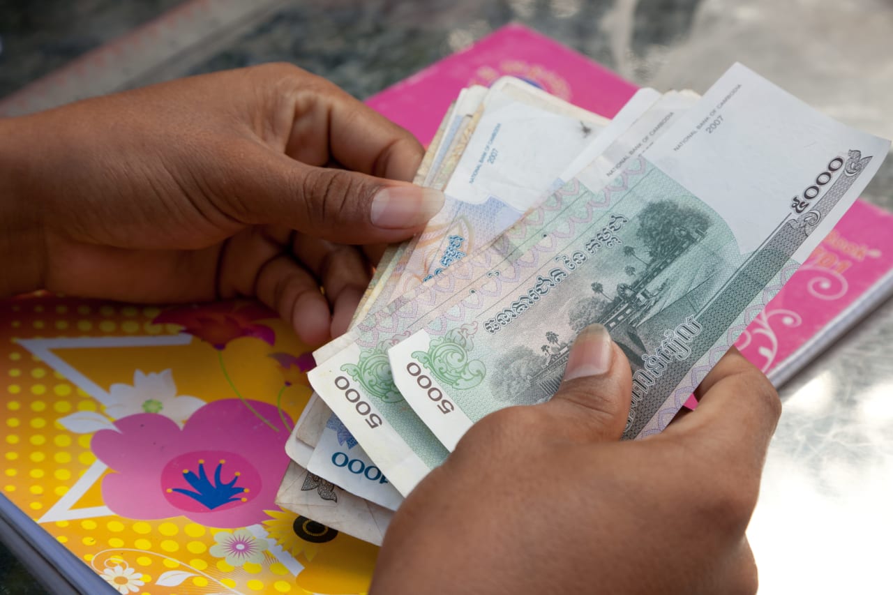 Las manos de una persona en Camboya sostienen billetes de diferentes tamaños y colores.