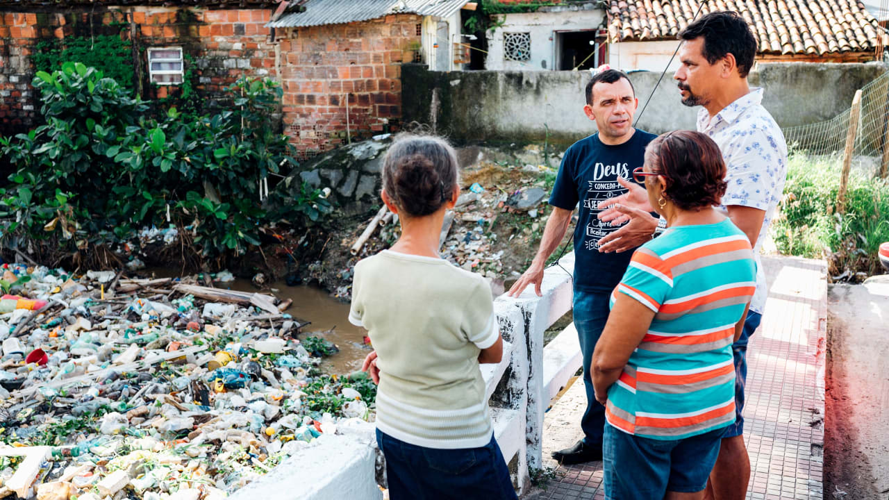 Four people stand on a bridge over a river filled with rubbish