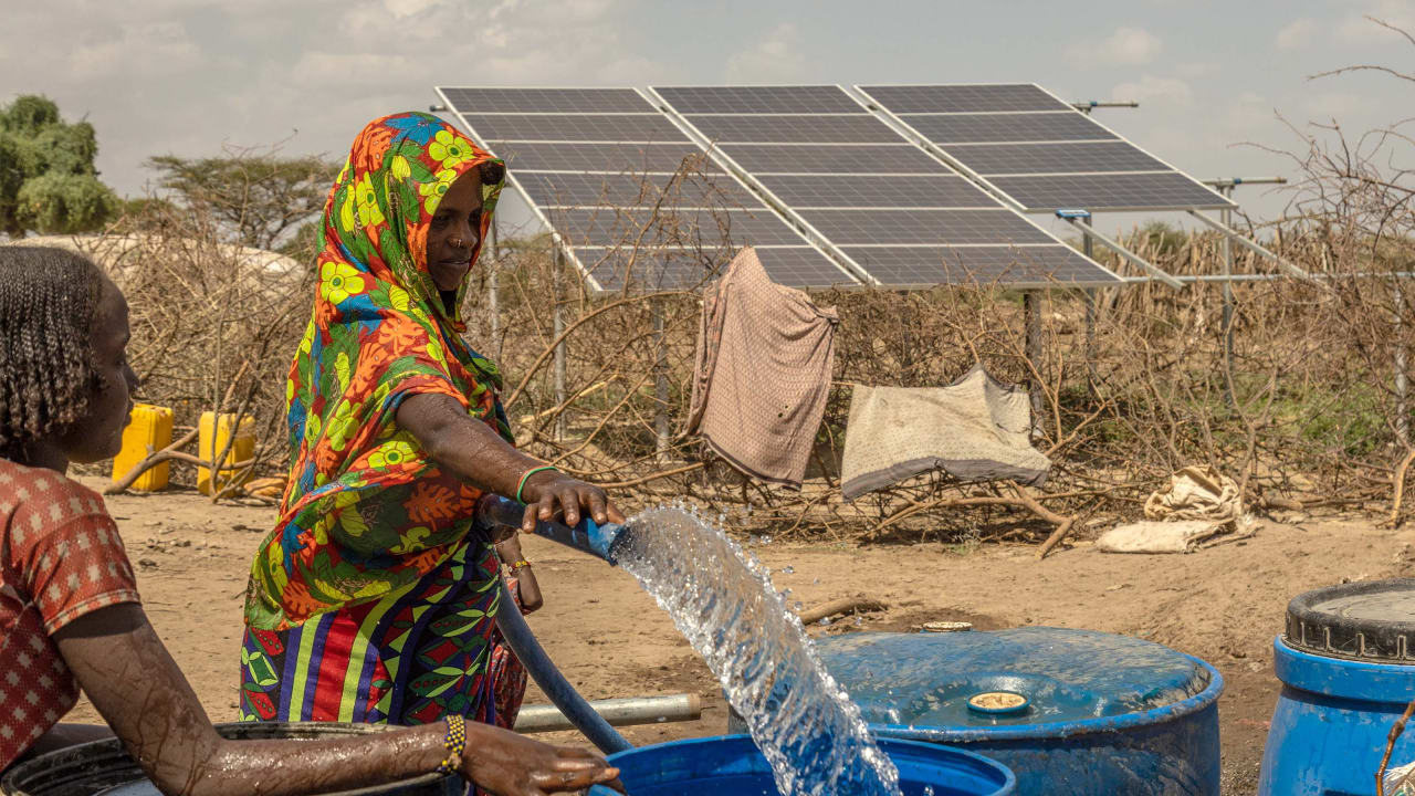 A woman in Ethiopia fills large plastic drums with clean water in front of an array of solar panels