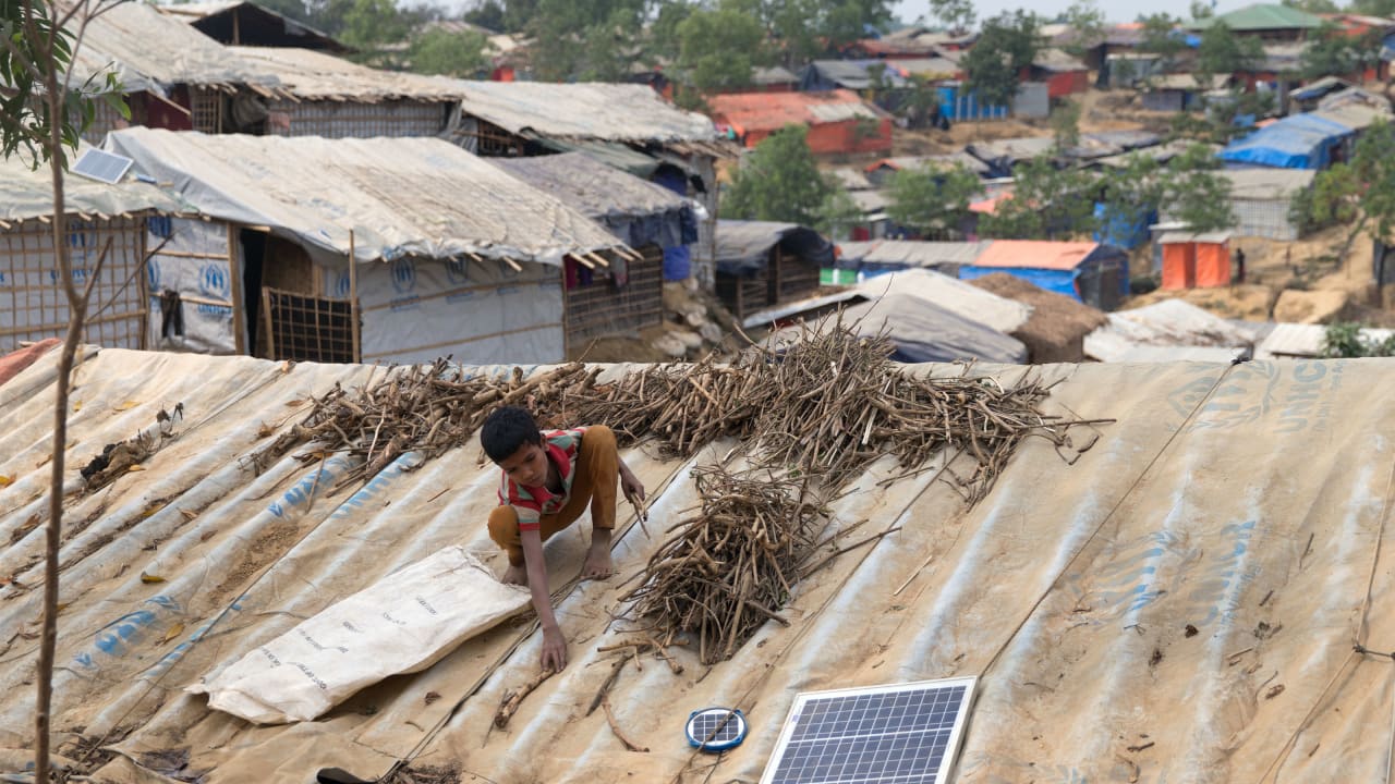 A child arranges firewood on the roof of his family tent, next to a solar panel, in a Rohingya camp in Bangladesh. 