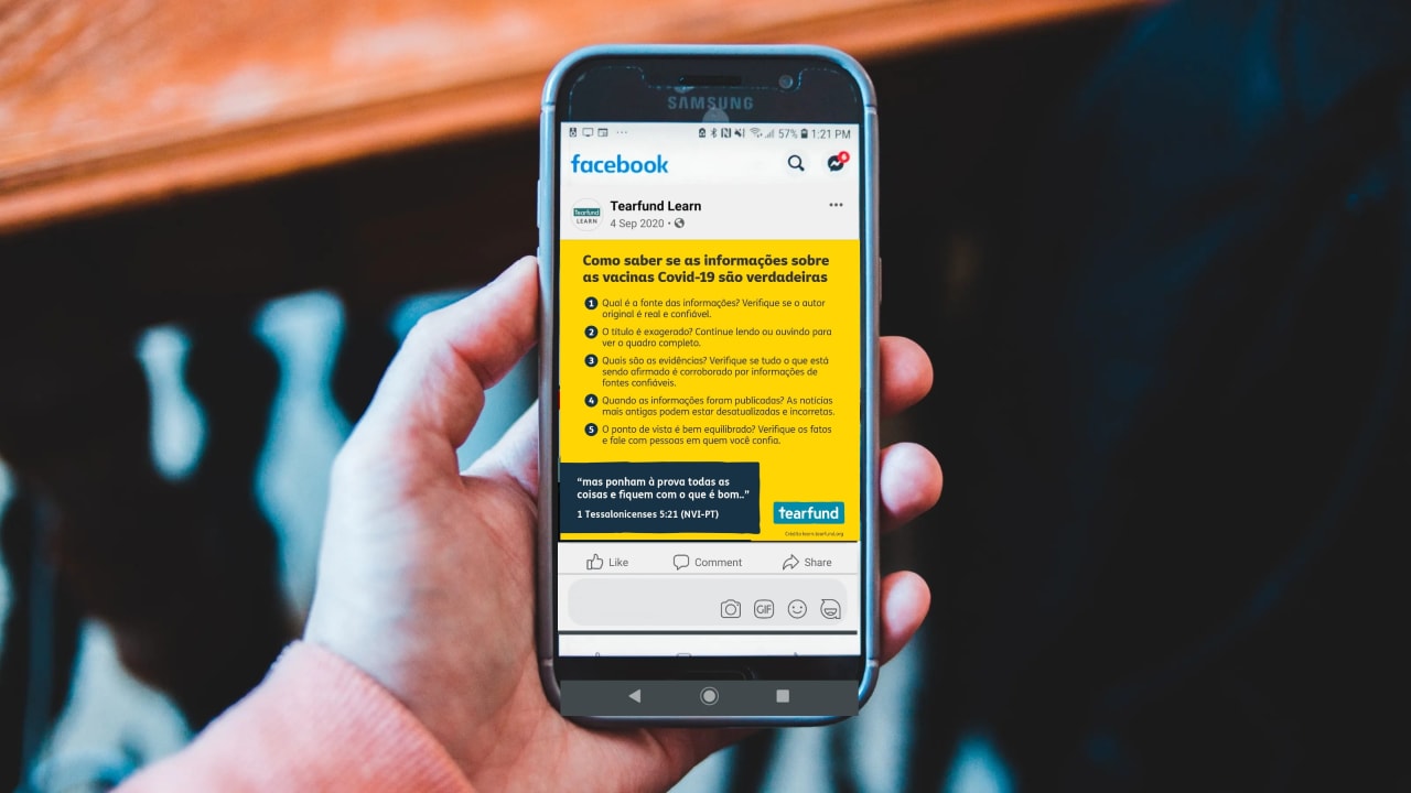 Uma mão segurando um telefone celular com informações úteis da Tearfund sobre a Covid-19 na tela