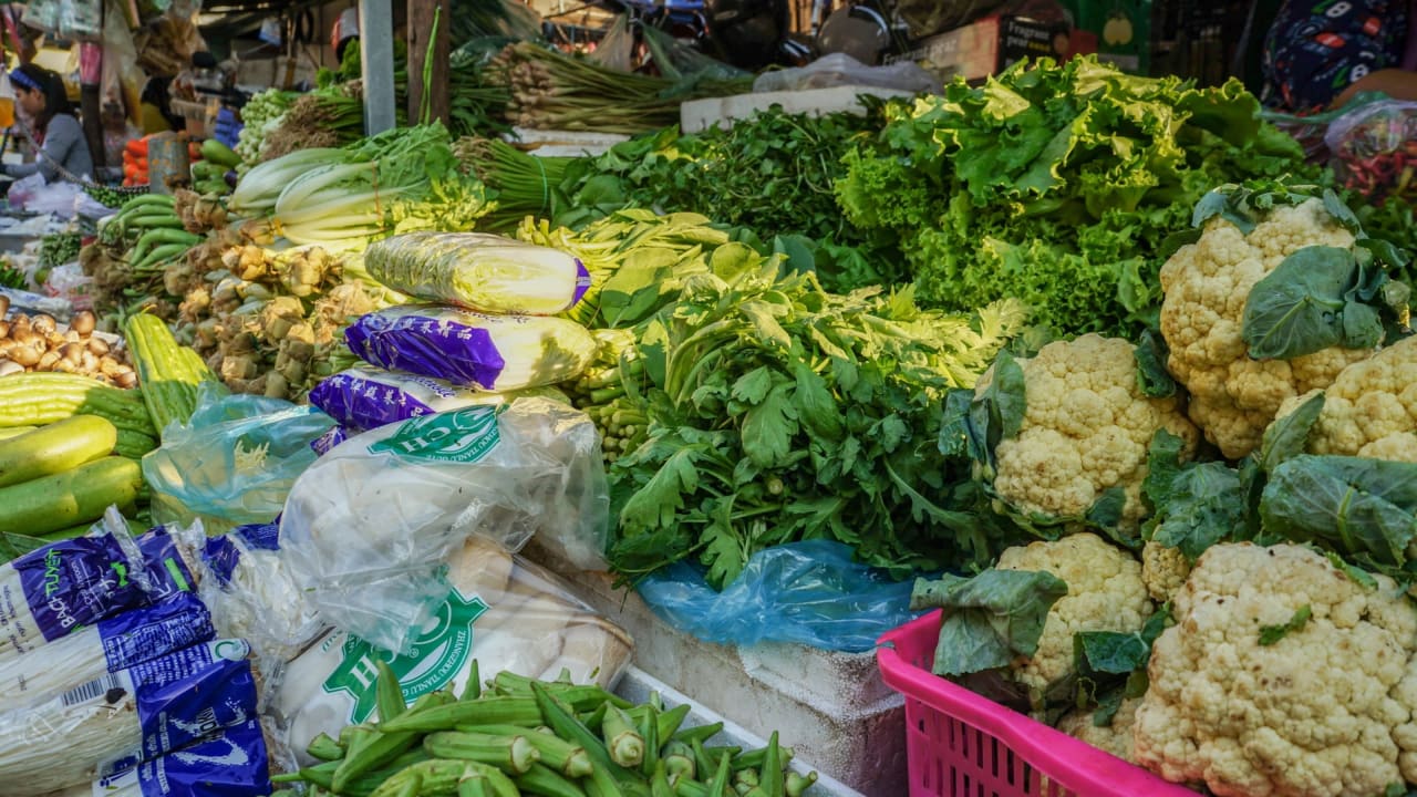 Un étalage de marché au Cambodge avec un éventail de fruits et de légumes verts.