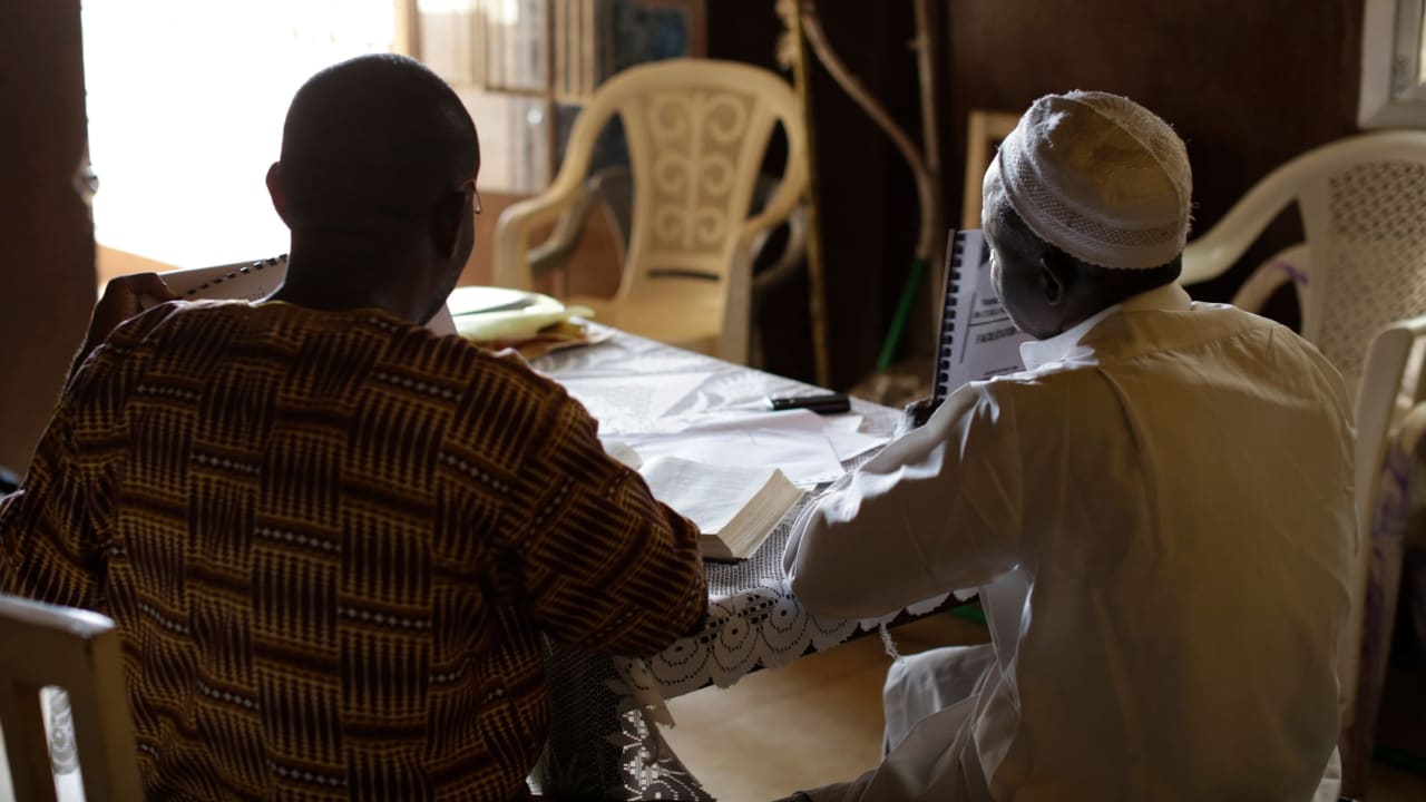 Deux chefs religieux de Sierra Leone sont assis à une table dans une pièce faiblement éclairée et discutent de leur réponse au virus Ebola.