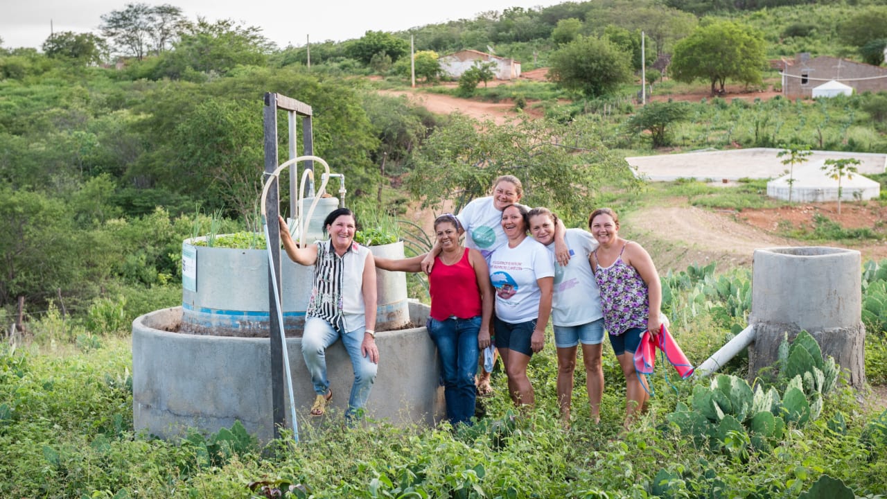 Five women from the local community stand next to a water well in a rural area