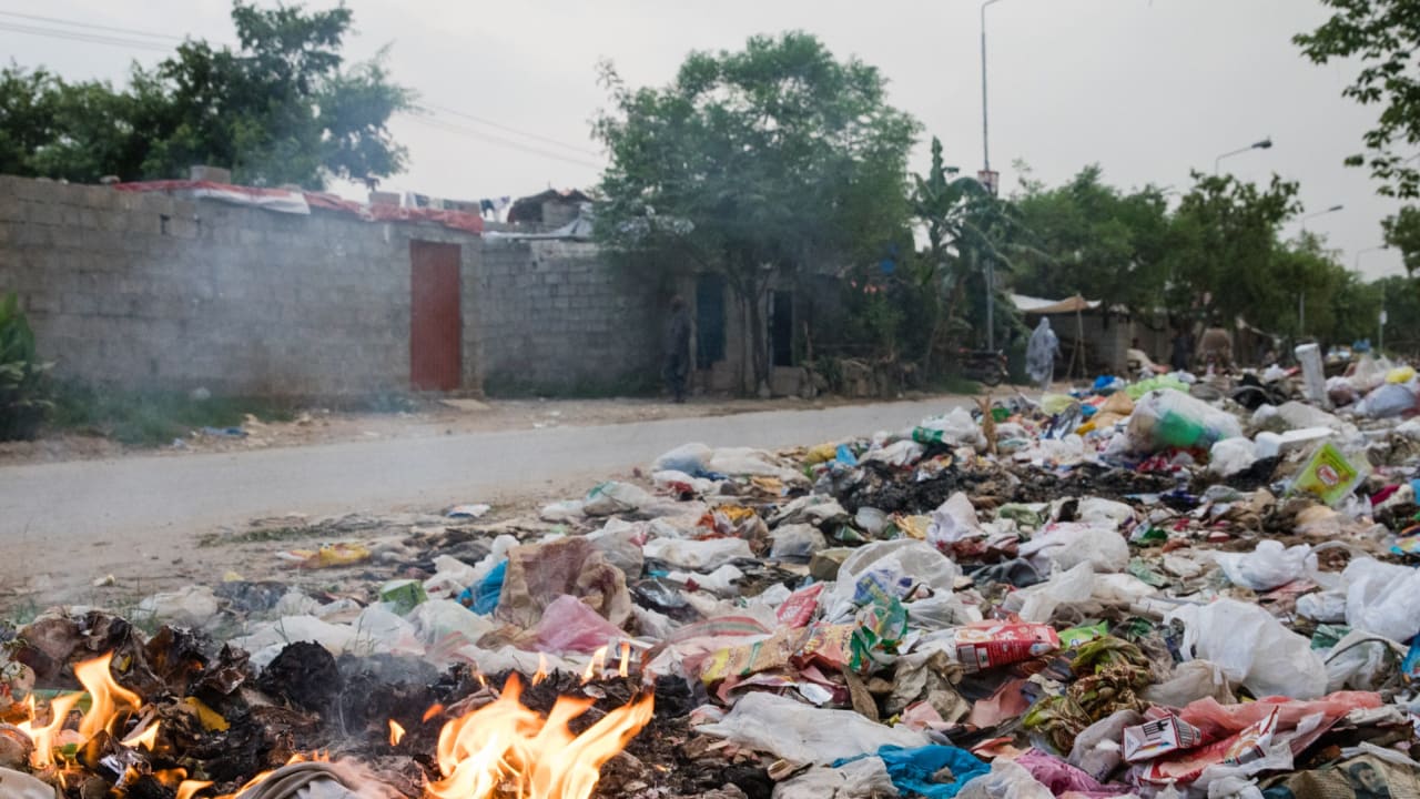 Des déchets brûlent sur le bord de la route dans un peuplement informel du Pakistan.