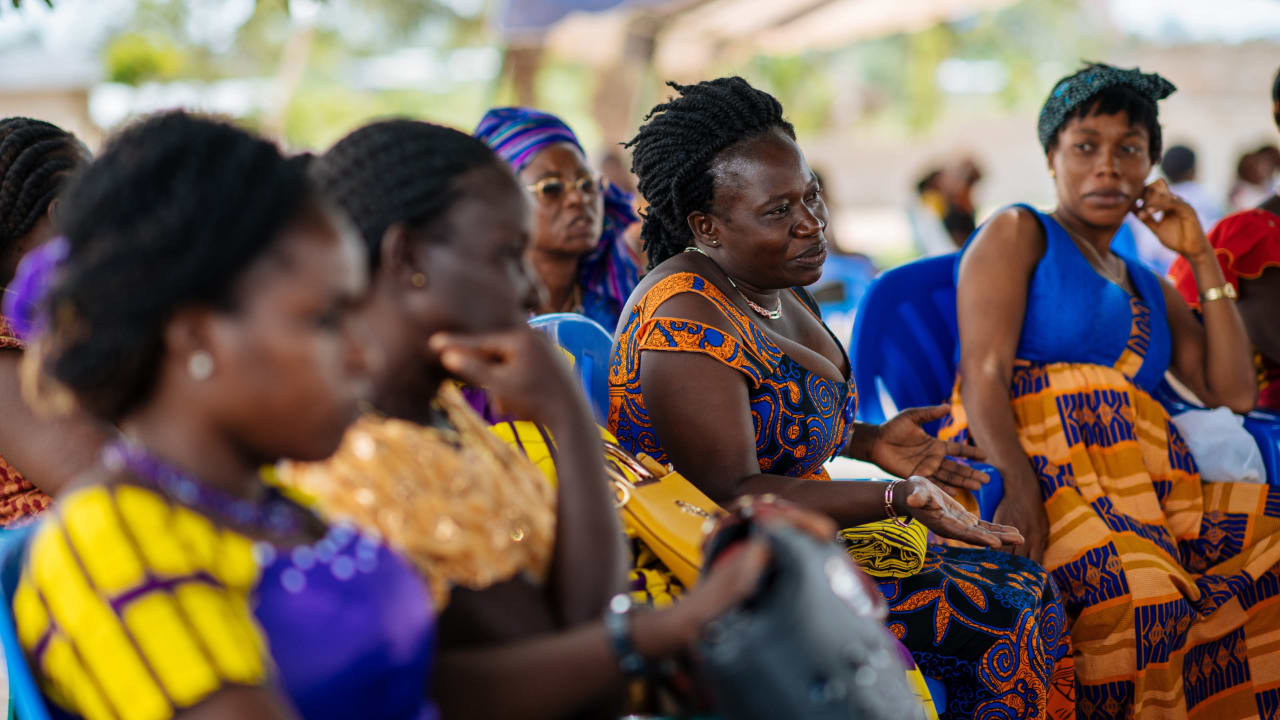 Quatro mulheres de Diégonefla, na Costa do Marfim, vestindo roupas tradicionais azuis e amarelas, sentadas lado a lado, sorrindo e discutindo a mobilização da igreja local