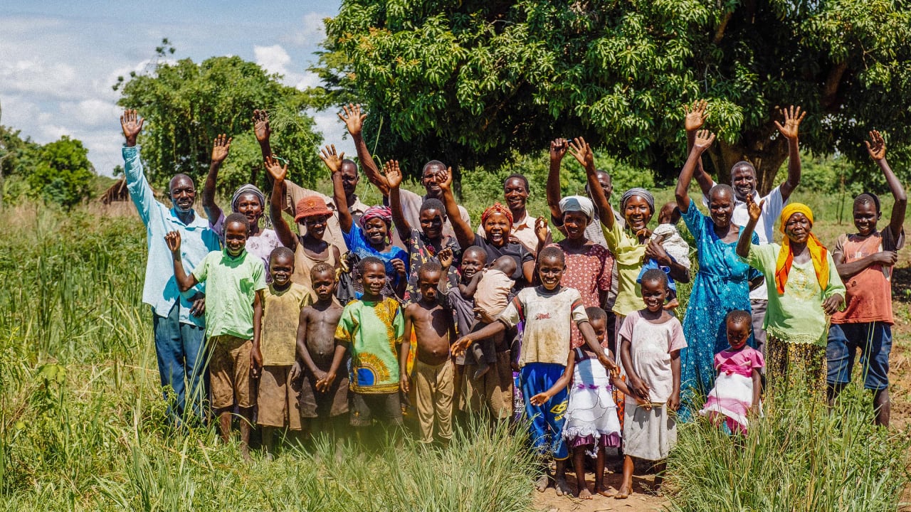 Des hommes, femmes et enfants, membres d’une communauté en Ouganda, en Afrique, sourient à la caméra en saluant de la main.