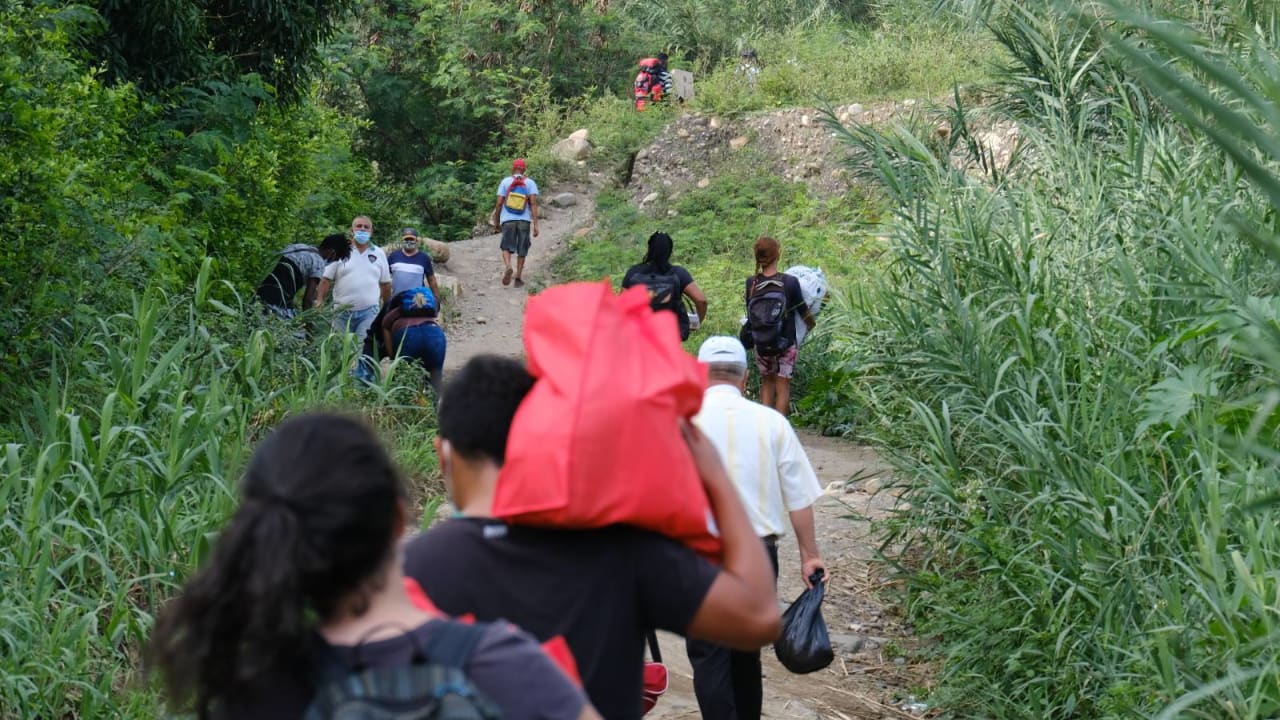 Un groupe de migrants du Venezuela marche le long du lit d’une rivière asséchée, portant des sacs à dos et des provisions, pour tenter de rejoindre la Colombie.