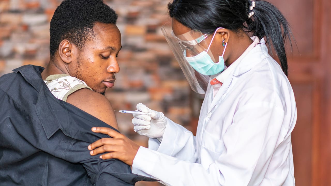 An African man receives a vaccine injection from a lady nurse