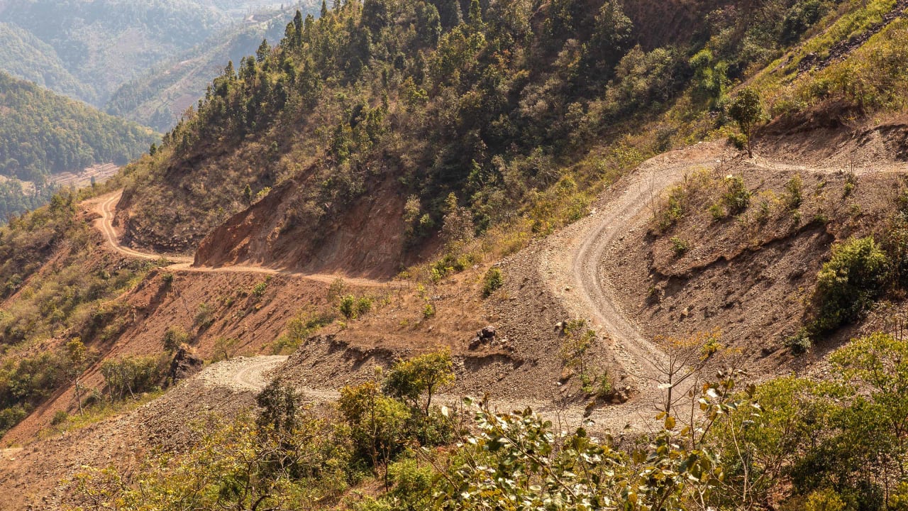 Un camino de tierra, empinado y sinuoso, sube por la ladera de una montaña en Nepal.