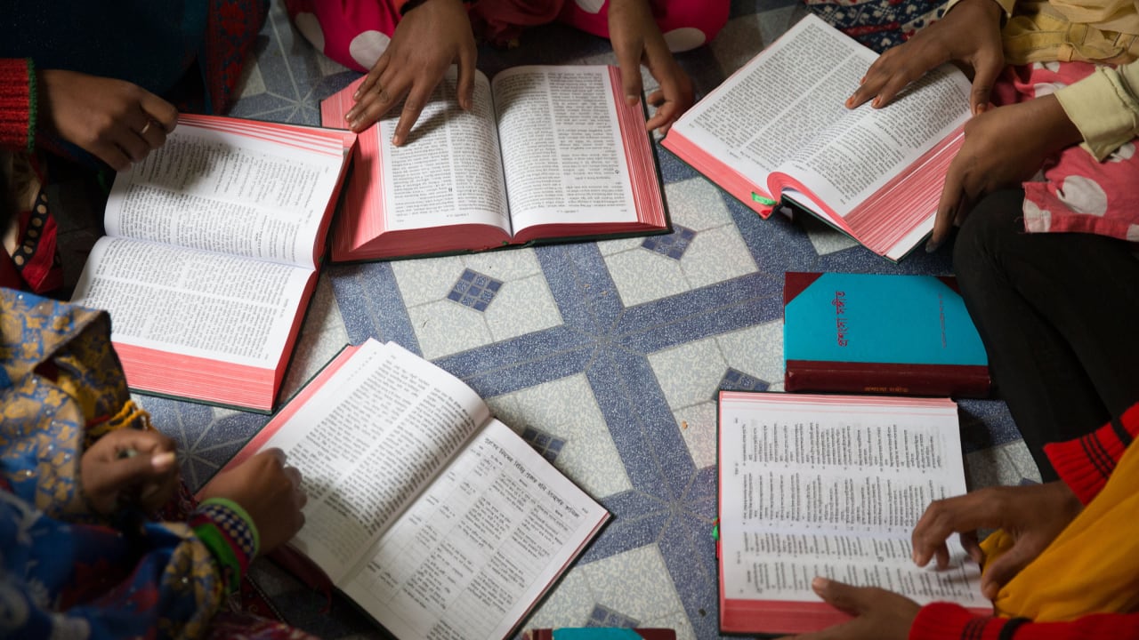 Un grupo de mujeres, arrodilladas en círculo en el suelo, leen cada una su Biblia