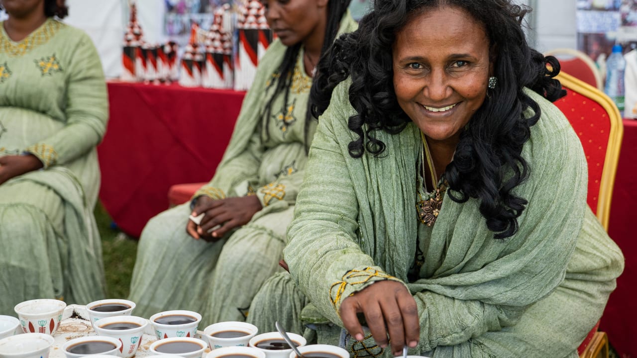 A smiling woman sitting in front of a table full of cups of coffee