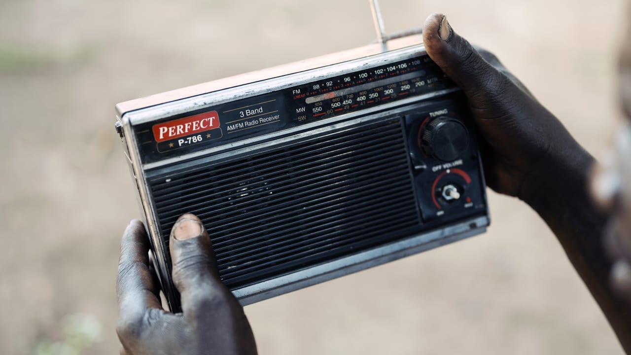Hands hold an old "Perfect" brand AM/FM radio with a tuning dial and antenna.
