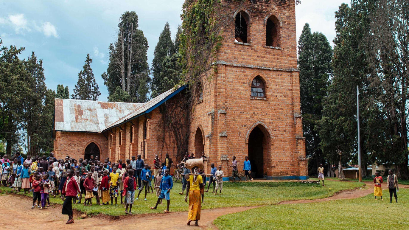 An old brick church in an African village setting with community members standing around outside.