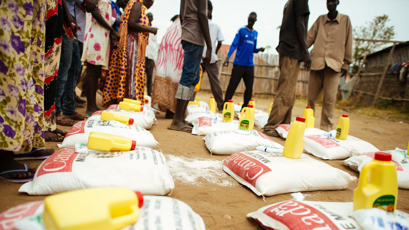 Aide alimentaire d’urgence disposée à même le sol, avec des personnes debout tout autour