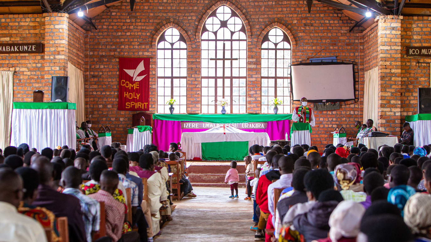 Vista interna de uma igreja africana cheia de pessoas, com uma criança pequena parada no corredor