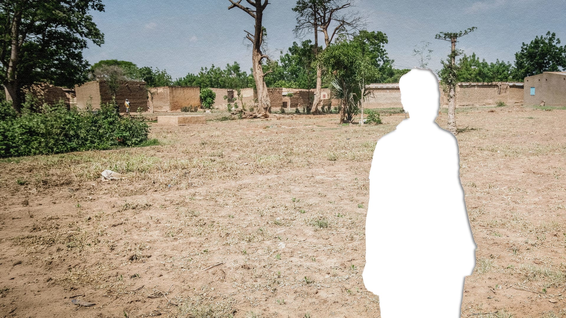A photograph of several buildings in the distance and a dry field in the foreground with a silhouette cut out of a person in white. 