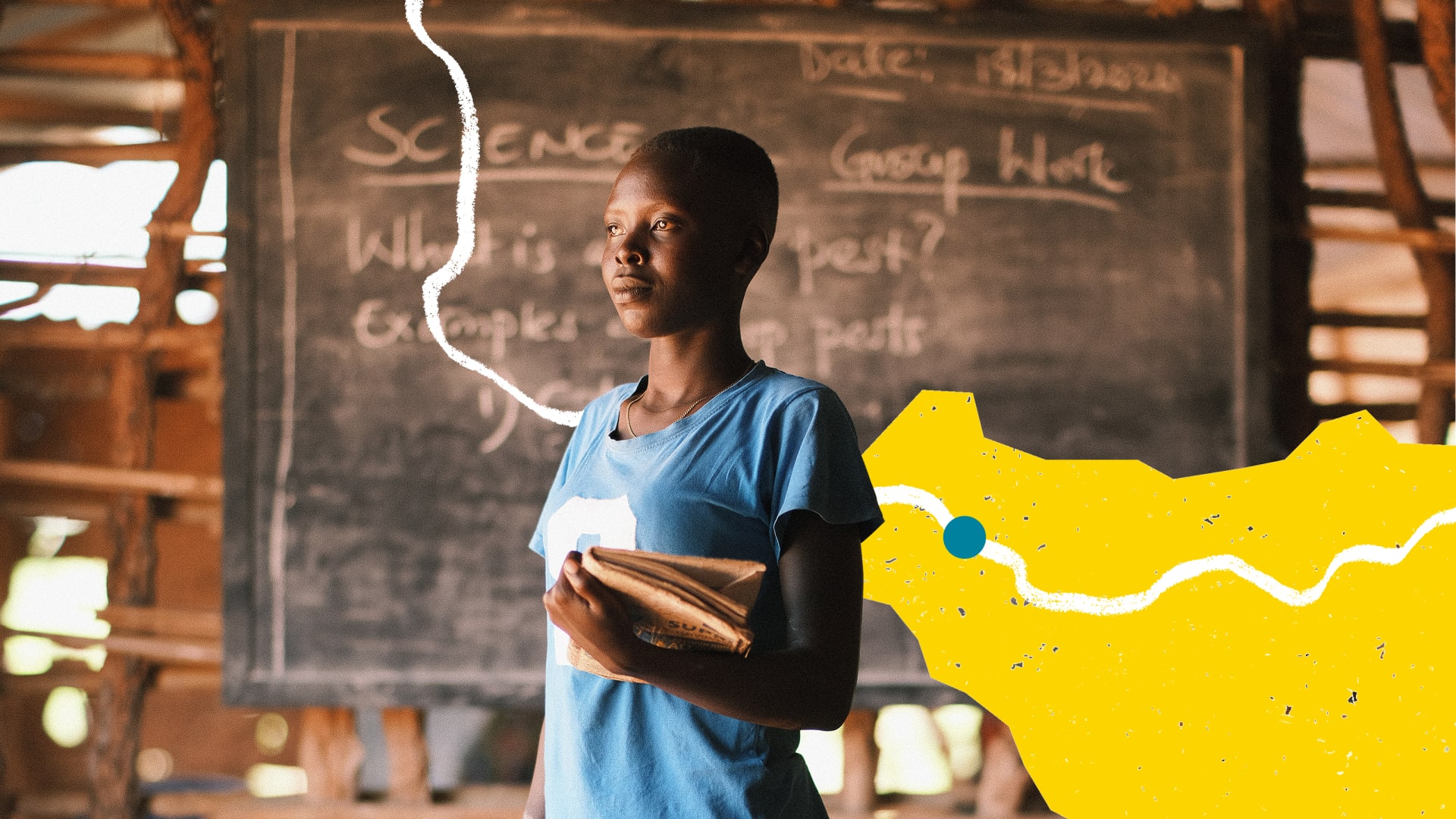 Young student stands with books in front of a classroom chalkboard.