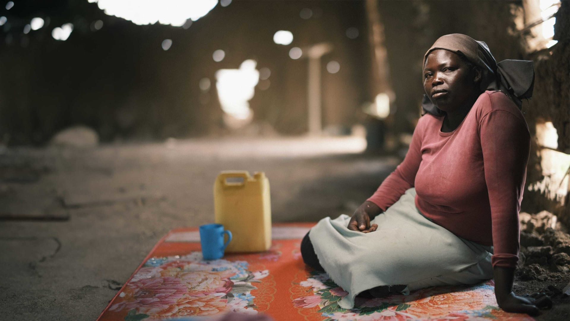 A woman is sitting in a dark room with light coming through holes in the walls around her.