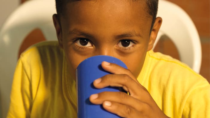A child wearing a yellow t-shirt drinks from a blue plastic cup in Colombia.