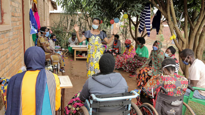 A group of people with disabilities in Rwanda sitting in a circle focused on a lady facilitator in the middle.