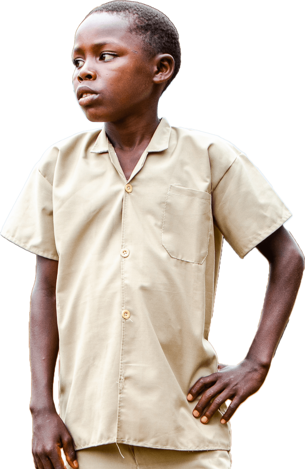 A young boy stands outside his school in Burundi with his hand on his hip looking proud