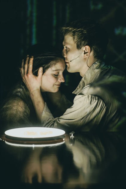 Na zdjęciu dwie osoby na scenie w bliskim uścisku. Jedna (Robert Ciszewski) trzyma drugą (Maria Wróbel) za głowę. Oświetlenie przyciemnione, tło nieostre.