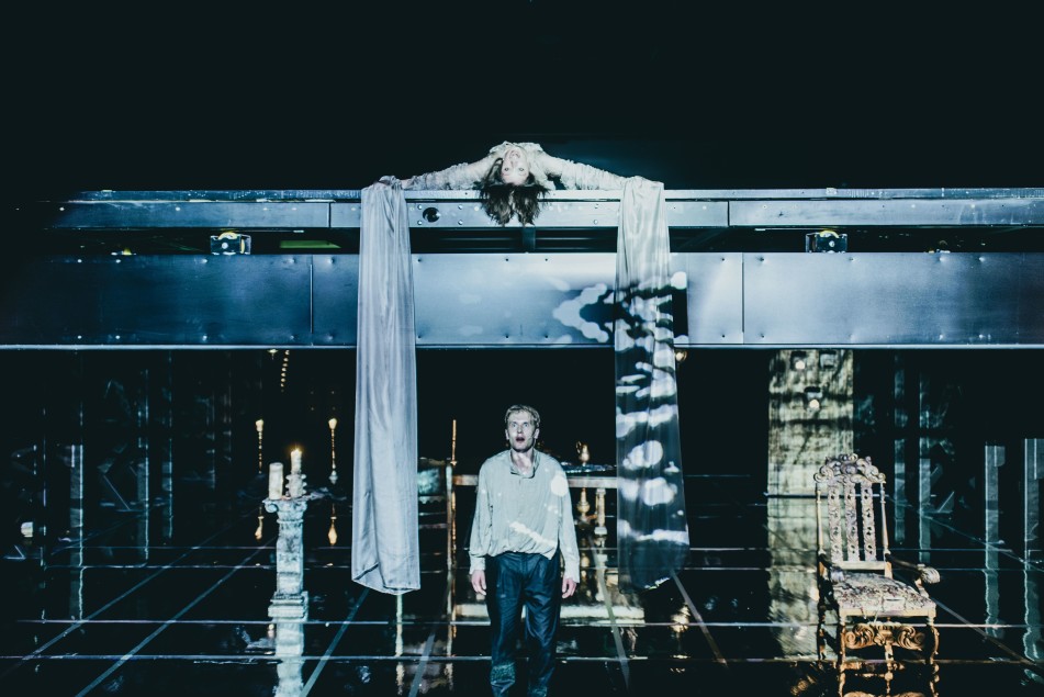 Na zdjęciu scena teatralna z dwoma poziomami. Na górnym leży osoba (Maria Wróbel) zwisająca głową w dół, na dolnym stoi druga osoba (Robert Ciszewski) patrząca w górę.