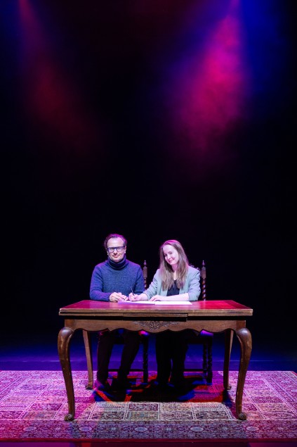 Kobieta i mężczyzna siedzą przy drewnianym stole, to pracownicy Teatru Wybrzeże: Anna Augustyniak i Radosław Paczocha. Podpisują list intencyjny.
