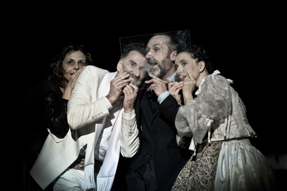 Czworo aktorów stoi blisko siebie, trzymając przy twarzach przezroczyste płytki; światło podkreśla ich mimikę.