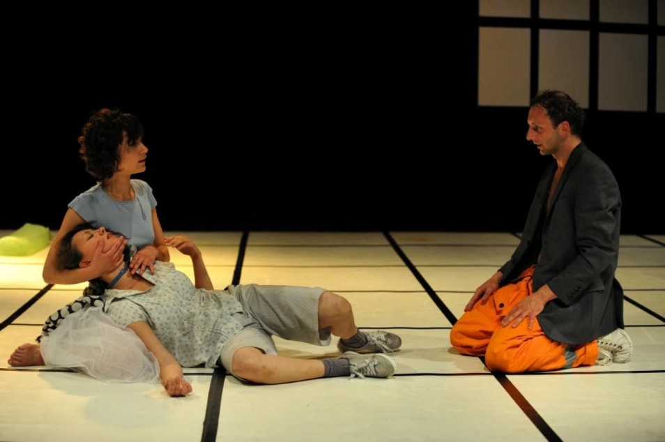 Kobieta podtrzymuje leżącą osobę, obok klęczy mężczyzna. Scena pełna emocji, wyraźny gest opieki i bezruchu.